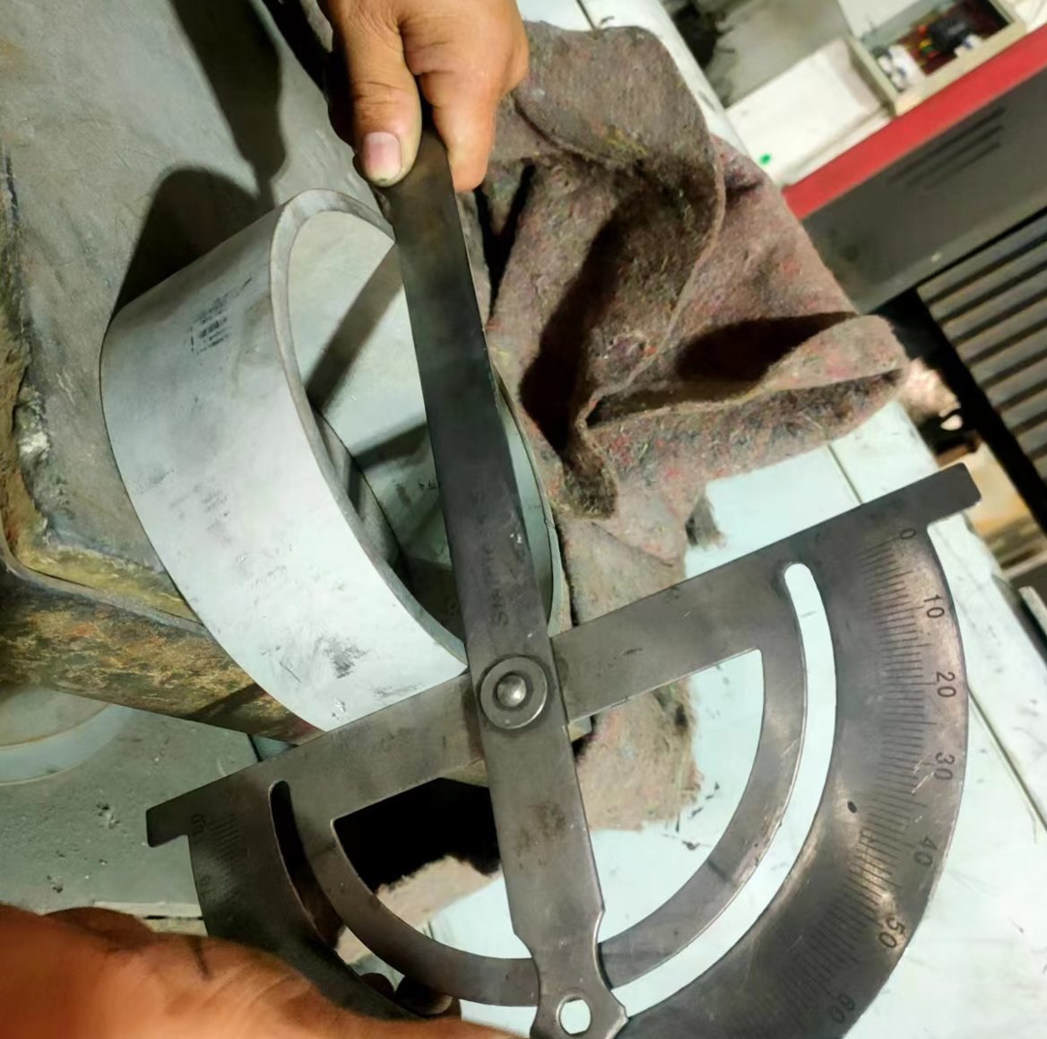 Operator checking the cut angle of a stainless steel pipe section with a protractor gauge